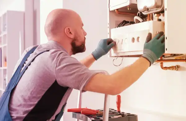 Tecnico con guanti verdi effettua la revisione caldaia in ritardo, regolando i comandi.
