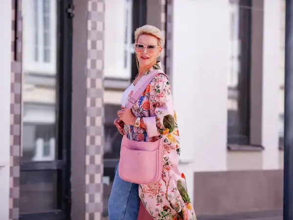 Kobieta w kwiecistym kimonie w stylu Moschino Bubble Gum, z różową torebką i okularami, idzie ulicą.