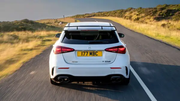 Biały Mercedes-AMG A45s pędzi po krętej drodze wśród wzgórz.