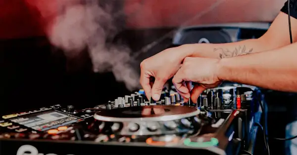 Mani esperte del dj sax mixano la musica, creando un'atmosfera vibrante con fumo e luci soffuse.