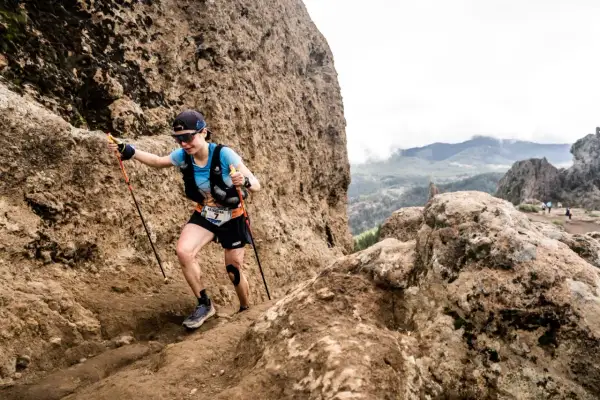 Katharina Hartmuth grimpe un sentier rocheux escarpé, bâtons en main, lors d'une course en montagne.