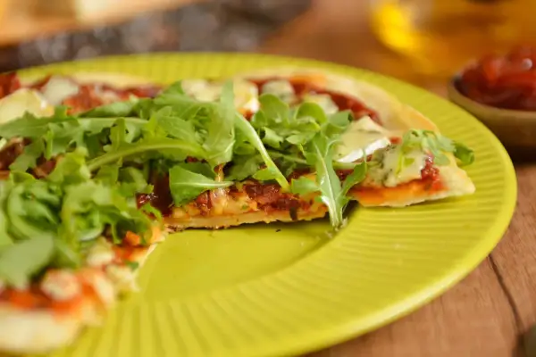 Pyszna pizza z patelni, z rukolą i serem, na żółtym talerzu.