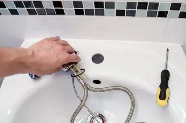 Hand montiert einen Wasserhahn, um das Waschbecken zu reparieren. Ein Schraubenzieher liegt bereit.