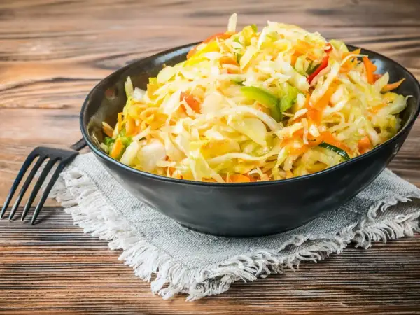 Kolorowa surówka z kiszonej kapusty inaczej, z dodatkiem marchewki, papryki i innych warzyw, podana w czarnej misce.