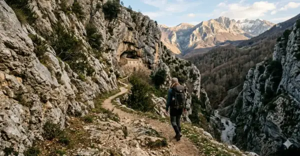 Escursionista su un sentiero roccioso, con un antico edificio incastonato nella roccia. Un viaggio che sembra un vero sentiero dello spirito tra montagne maestose.