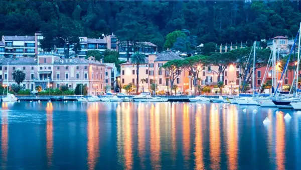 Serata a Toscolano Maderno: hotel illuminati, barche a vela e riflessi sull'acqua creano un'atmosfera magica.