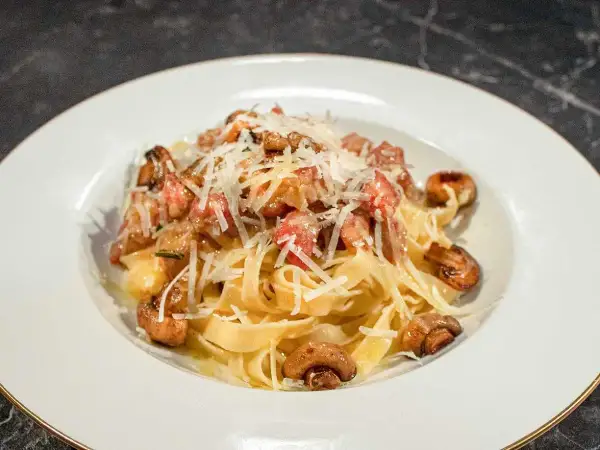 En tallrik med pasta alla boscaiola, toppad med riven parmesan och champinjoner.