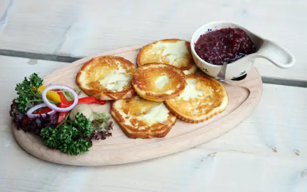 Smażony oscypek z żurawiną, podany z sałatką i pieczywem, na drewnianej desce.