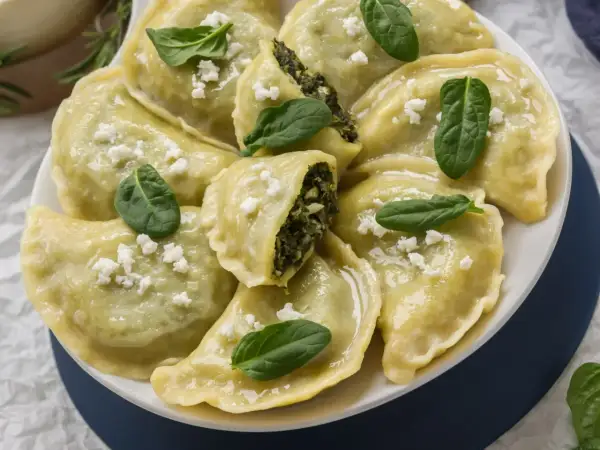 Pyszne pierogi ze szpinakiem i fetą, udekorowane świeżymi listkami szpinaku.