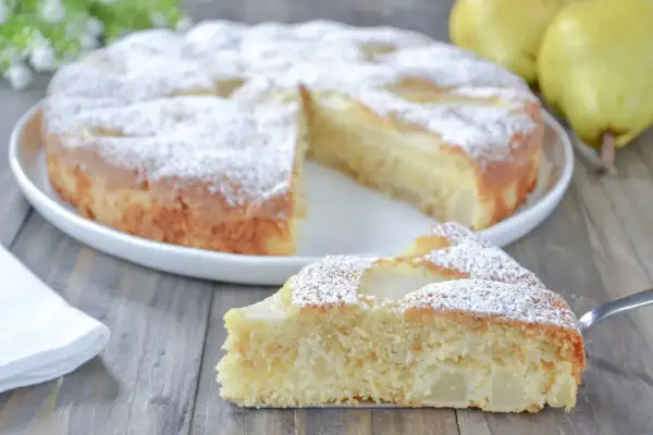 Una fetta di torta pere soffice e profumata, cosparsa di zucchero a velo, su un tavolo di legno.