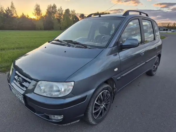 Szary Hyundai Matrix na tle zachodzącego słońca i zielonej łąki.