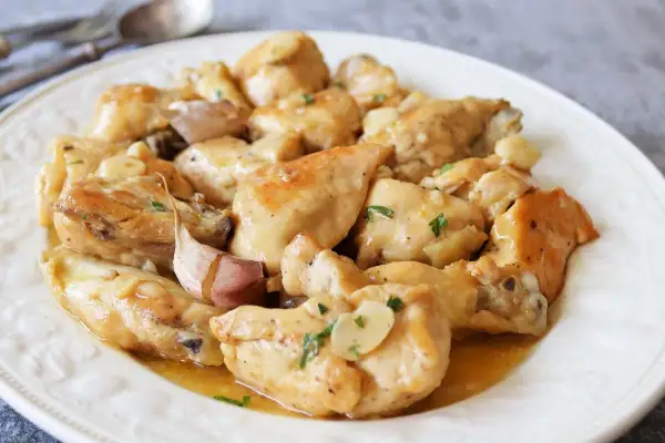 Sabroso pollo al ajillo al horno, jugoso y dorado, servido en un plato blanco con trozos de ajo y perejil picado.