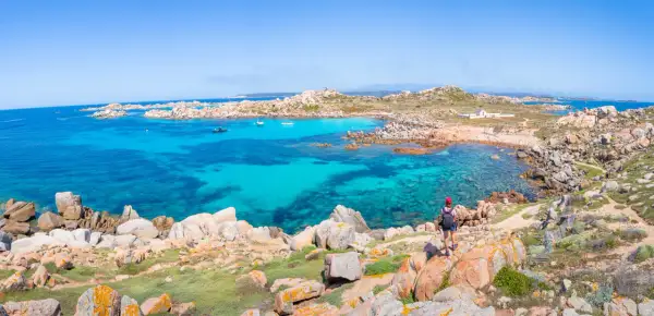 Vue panoramique de l'île Lavezzi, avec ses eaux turquoise cristallines, ses rochers granitiques et une randonneuse admirant le paysage.