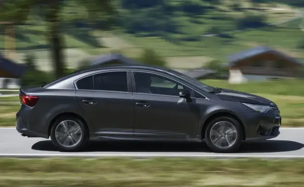 Ciemnoszara Toyota Avensis 2.0 D4D w ruchu, z rozmytym tłem górskiego krajobrazu.