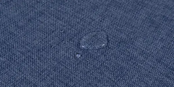 Gocce d'acqua su tessuto blu, dimostrando l'efficacia del lavaggio antimacchia in lavatrice.