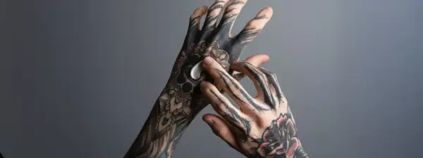 Hände mit detaillierten Tätowierungen, die mit einer weißen Creme eingerieben werden. Die tattoo tiefe der Muster wird durch die Pflege betont.