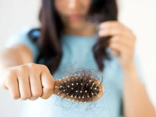 Mujer preocupada por la caída de pelo postparto, mostrando un cepillo lleno de cabello.