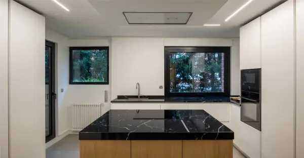 Cocina moderna con **fregadero en isla** de mármol negro y encimeras a juego. Muebles blancos y electrodomésticos integrados.