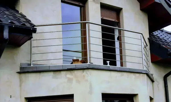 Nowoczesna poręcz ze stali nierdzewnej na balkonie, z widokiem na okna i dachówki.