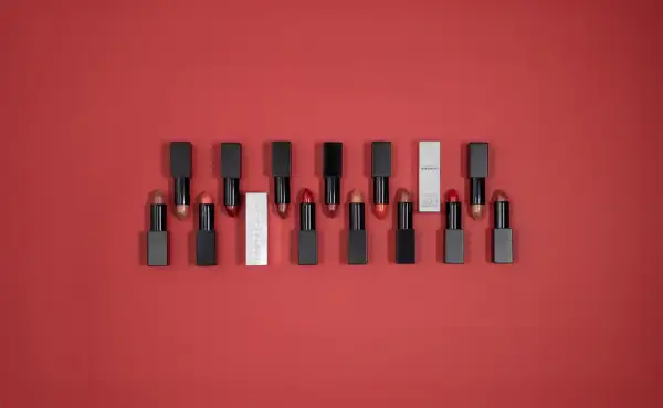 Une collection de rouges à lèvres aux teintes variées, dont un rouge rose éclatant, sur fond rouge.