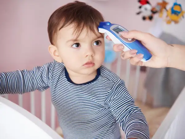 Mama mierzy temperaturę niemowlaka termometrem bezdotykowym. Dziecko ma na sobie pasiasty pajacyk.
