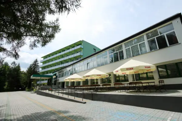 Zielony budynek sanatorium prywatnie, z tarasem i parasolami.
