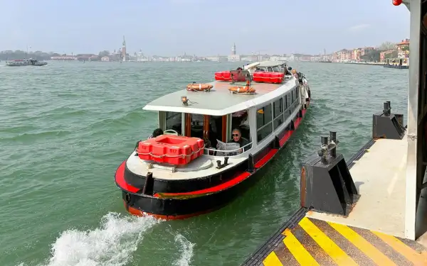 En man läser tidningen på en av båtarna i Venedig. I bakgrunden syns stadens silhuett.