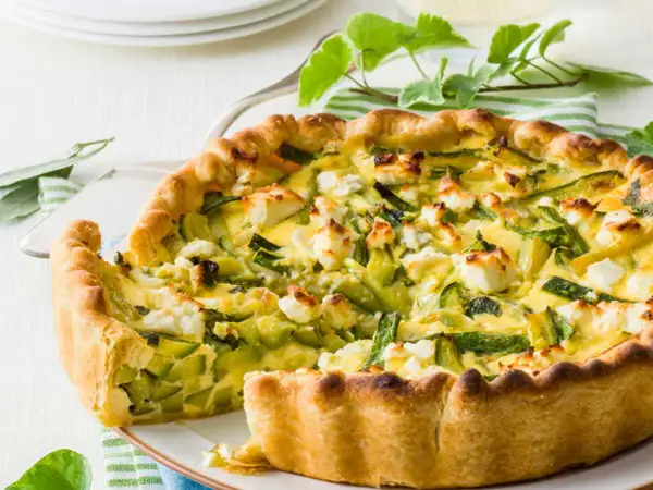 Tarte ricotta courgette dorée, garnie de dés de fromage blanc et de lamelles de courgettes vertes.