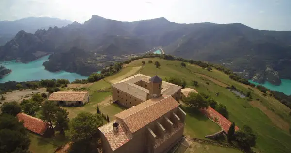 Edificio histórico en la Serra de Busa, con un lago turquesa y montañas al fondo.