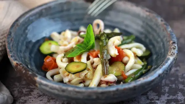 Deliziosa insalata di mare con verdure fresche: calamari, pomodorini, zucchine e asparagi, guarnita con basilico.