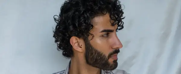 Hombre con un moderno peinado chino, cabello rizado oscuro y barba cuidada.