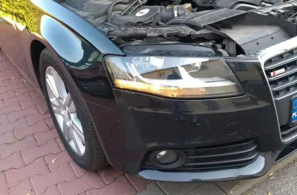 Audi A4 B8 przód: wymiana żarówki kierunkowskazu. Silnik odsłonięty, maska podniesiona.