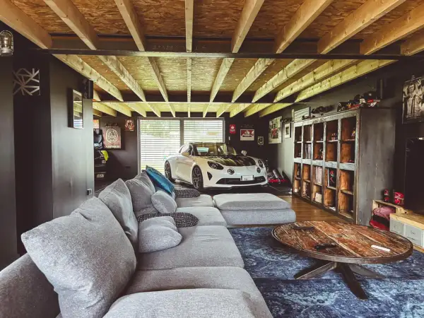 Aménager son garage : un canapé confortable, une voiture de sport blanche et des étagères remplies d'objets de collection.