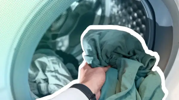 Hand lädt grüne Kleidung in eine Waschmaschine. Zeit, die neue Kleidung zu waschen und sie frisch zu machen.