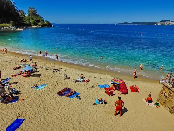 Gente disfrutando del sol y el mar en la playa Portocelo. Arena dorada, aguas turquesas y un día perfecto para relajarse.