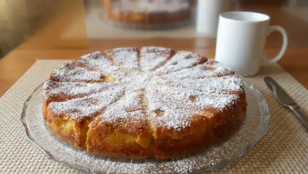 Gâteau fondant aux pommes et mascarpone, saupoudré de sucre glace, prêt à être dégusté avec une tasse de café.
