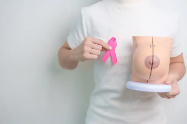 Dłoń trzyma różową wstążkę obok modelu piersi, symbolizując nadzieję po mastektomii z rekonstrukcją.
