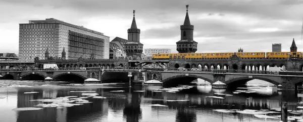 Gelbe U-Bahn fährt über die Oberbaumbrücke in Berlin. Im Vordergrund treibt Eis auf dem Wasser.