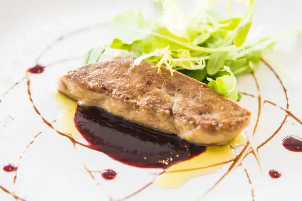 Un morceau de foie gras poêlé, servi avec une sauce aux fruits rouges et une salade verte. Une recette raffinée pour un plat d'exception.