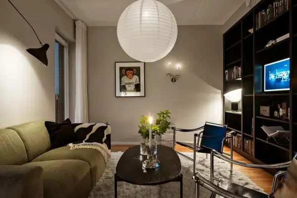 Mysig lounge med en grön soffa, svart soffbord och en bokhylla. Riktat ljus från en vägglampa skapar en varm atmosfär.