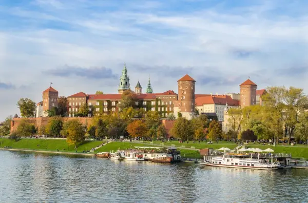 Zabytkowe miasto nad Wisłą, Wawel w jesiennej odsłonie, z łodziami cumującymi przy brzegu.