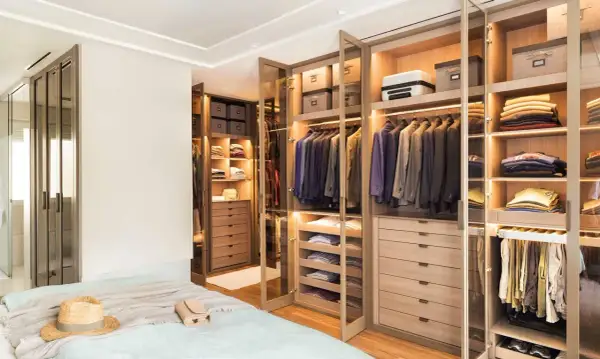 Armarios a medida con puertas de cristal y madera, llenos de trajes, ropa doblada y accesorios.