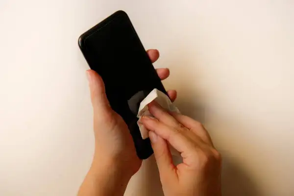 Dłonie czyszczą ekran telefonu chusteczką. Dowiedz się, czym wyczyścić ekran telefonu, by był lśniący i bez smug.