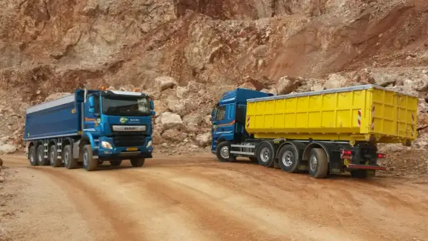 Deux camions bleus, un avec une benne jaune, circulent sur un chemin de carrière. Le prix du km camion 26 tonnes est une donnée clé pour ces transports.