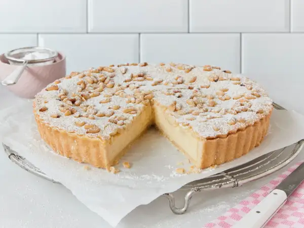 Eine köstliche Torta della Nonna, bestäubt mit Puderzucker und Pinienkernen, wartet darauf, angeschnitten zu werden.