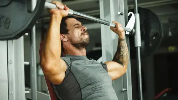 Mann hebt mit konzentriertem Gesichtsausdruck eine Langhantel im Fitnessstudio, ein intensiver 1 satz training.