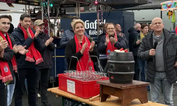 Menschen mit roten Schals klatschen bei Ruppichteroth Veranstaltungen. Eine Frau mit blonden Haaren steht im Mittelpunkt, daneben ein Mann mit Mikrofon.