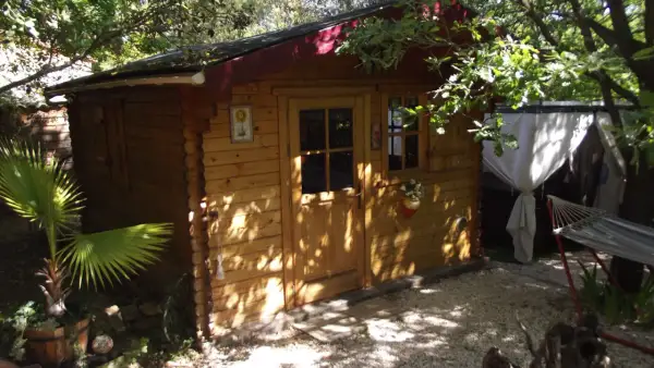 Charmante cabane en bois, nichée sous les arbres. Un hamac invite à la détente à côté.
