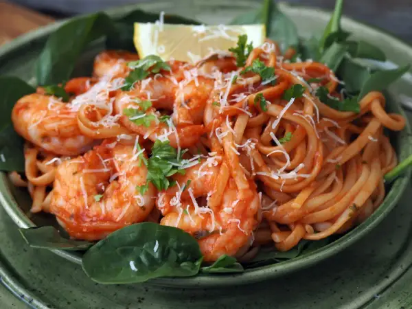 En skål med pasta pomodoro med räkor, toppad med riven ost och färsk persilja. En citronklyfta vilar ovanpå.