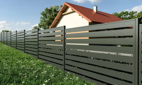 Nowoczesne ogrodzenie panelowe w ciemnoszarym kolorze, z drewnianymi wstawkami, otacza dom z czerwonym dachem. Idealne rozwiązanie, by poznać koszt ogrodzenia panelowego.